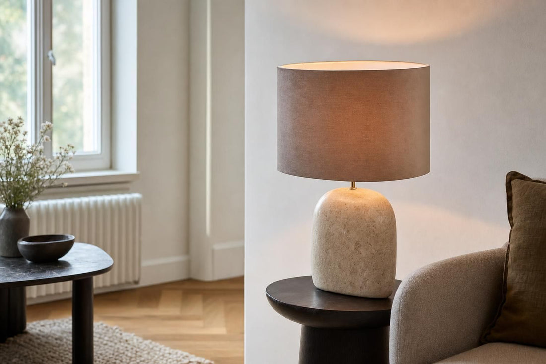 Ovale taupe velours lampenkap op een lampenvoet naast een tafel